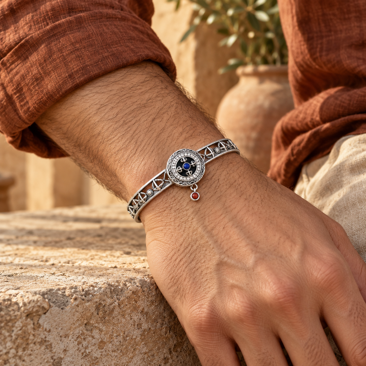 Men's Blue Wheel Cuff in Sterling Silver – contextual scene, on wrist beside stone with a rust linen sleeve