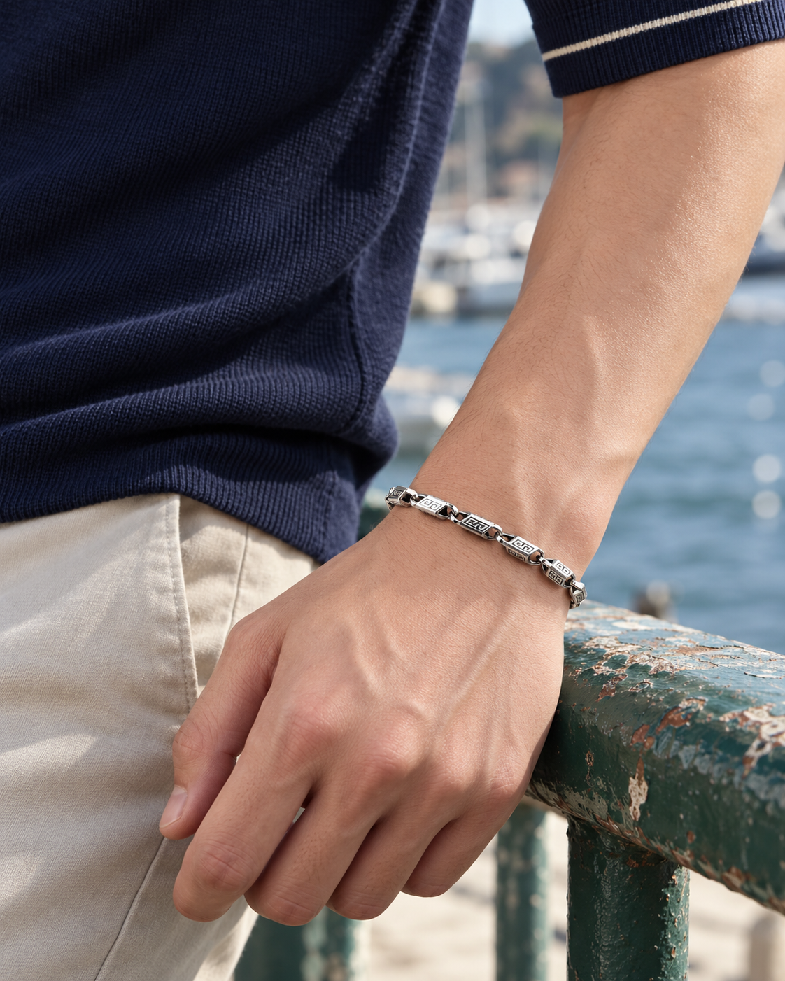 Men's Meander Block Sterling Silver Link Bracelet in Sterling Silver – contextual scene, on wrist with a navy knit polo beside the harbour