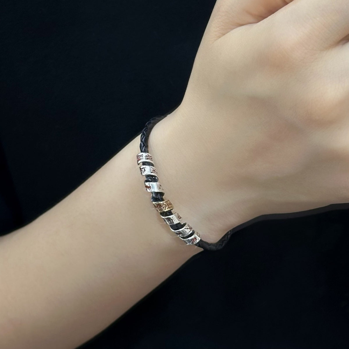 Men's Seven Glyph Braid Bracelet in Sterling Silver and Black Faux Leather – contextual scene, on wrist against plain black fabric