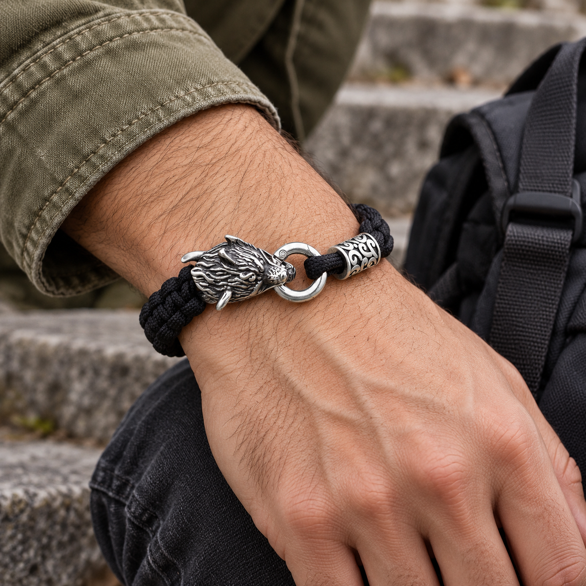 Men's Wolfhead Paracord Bracelet in black paracord and stainless steel – contextual scene on wrist with olive canvas sleeve