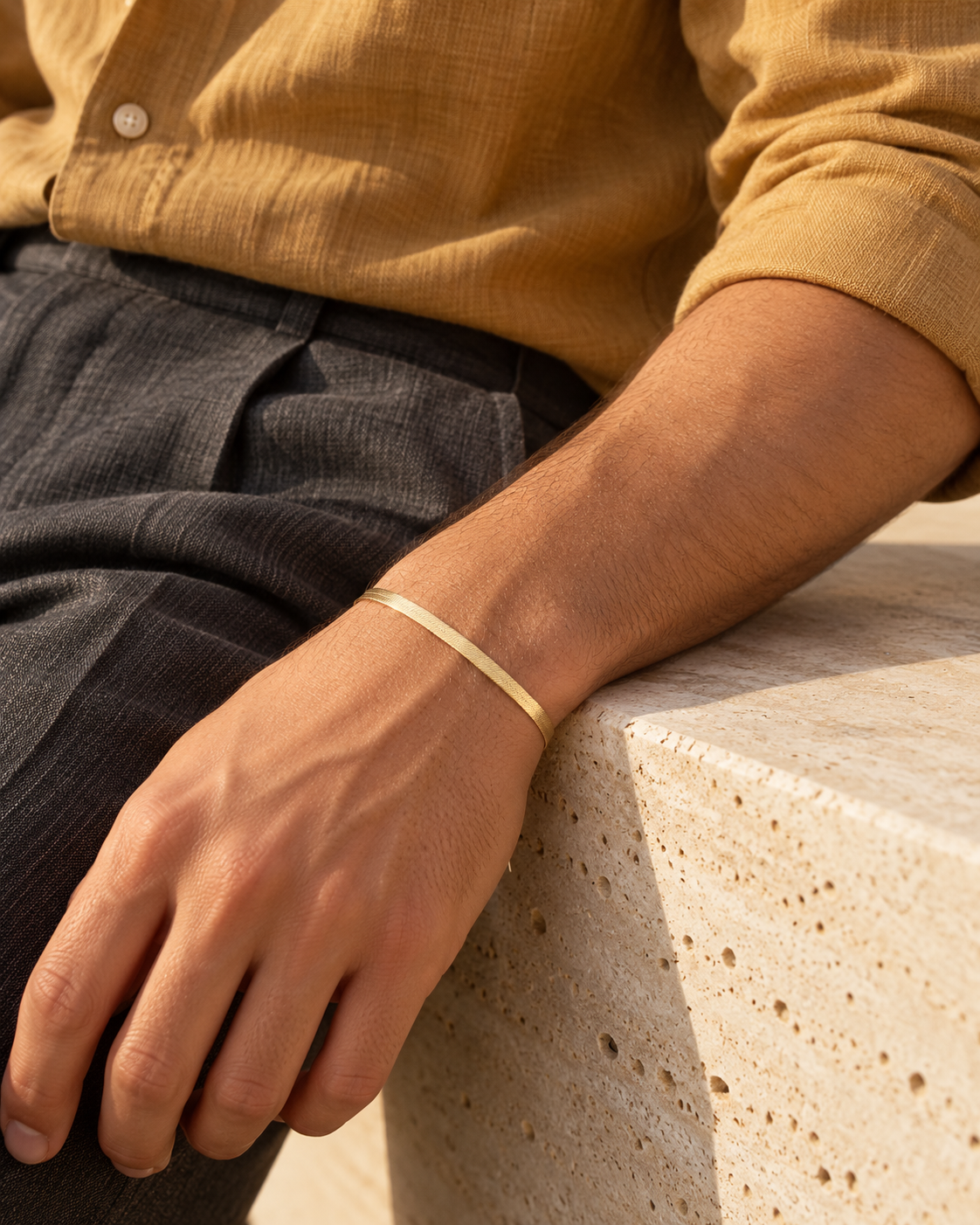 Men's Fine Herringbone Sterling Silver Bracelet in Gold-Tone Sterling Silver – contextual scene, on wrist with ochre linen at a gallery bench