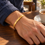 Men's Meander Band Bangle in 18K Gold Plated Steel – contextual scene, on wrist at a walnut table
