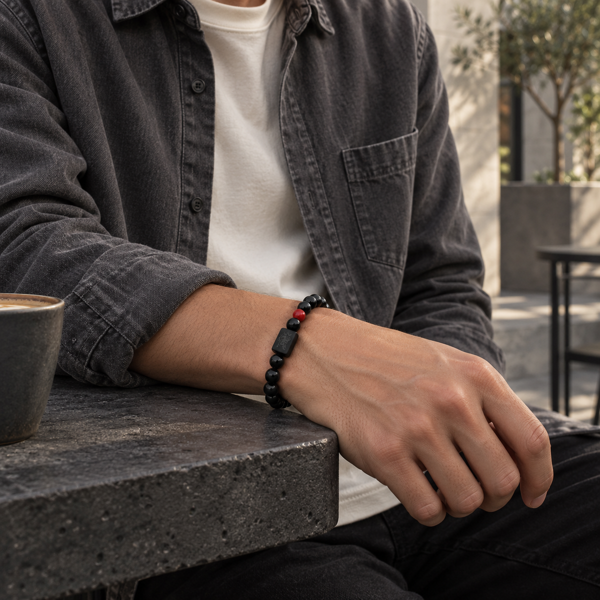 Red Lion Bead Cord Bracelet — contextual scene, charcoal overshirt in a courtyard